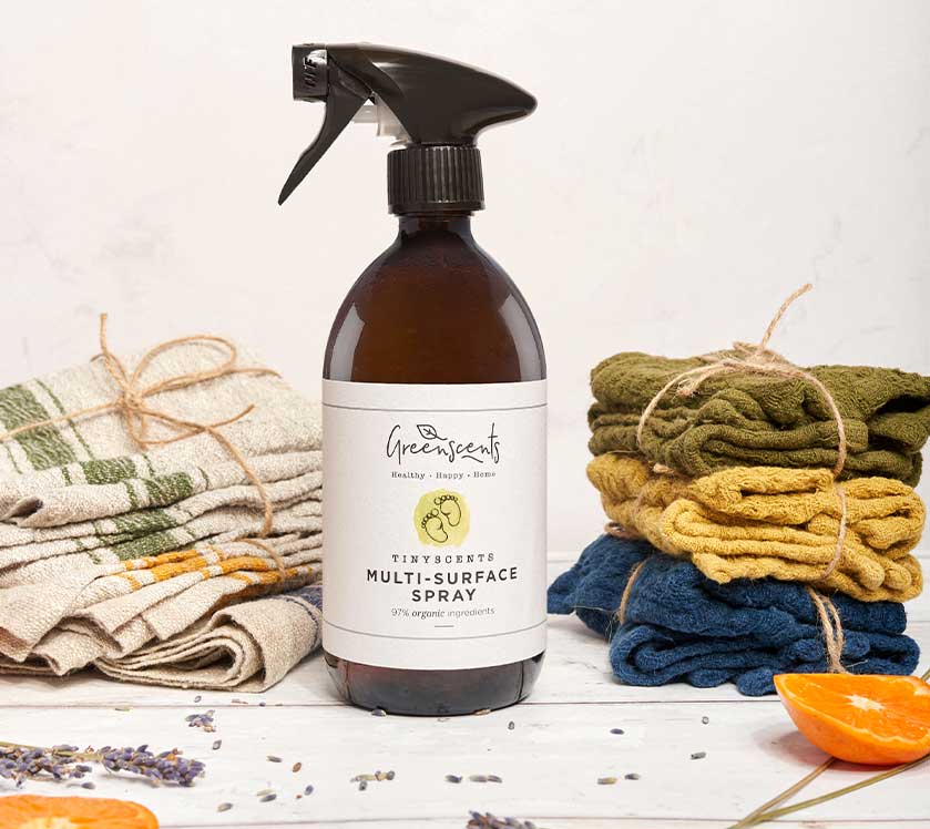 Brown spray bottle labeled 'GreenScents' with cloths and oranges on a white background
