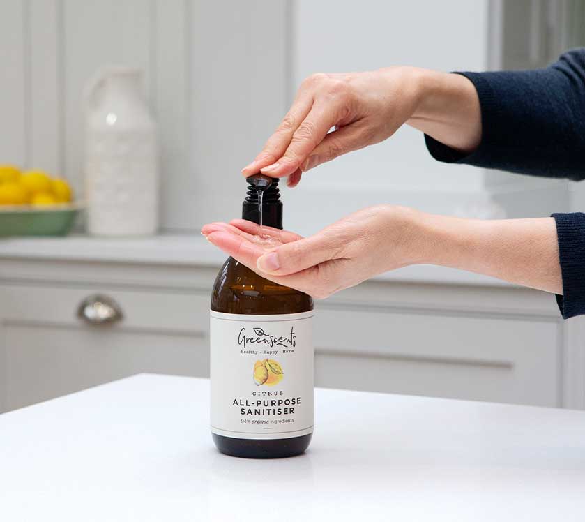 Person using a bottle of greenscents all-purpose sanitizer on a kitchen counter.