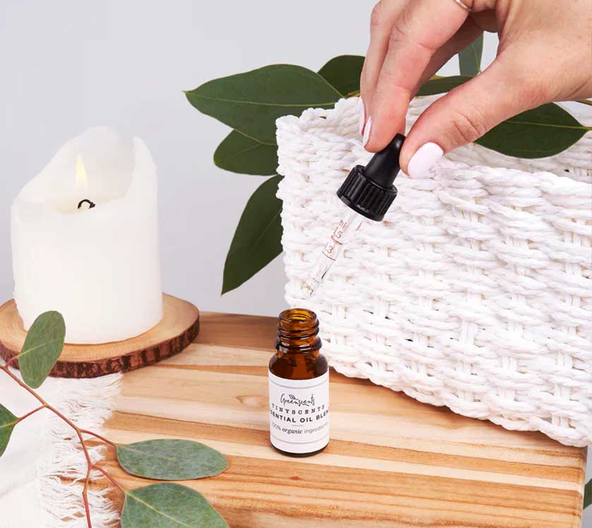 Hand using a dropper to add essential oil into a bottle with a candle and leaves in the background