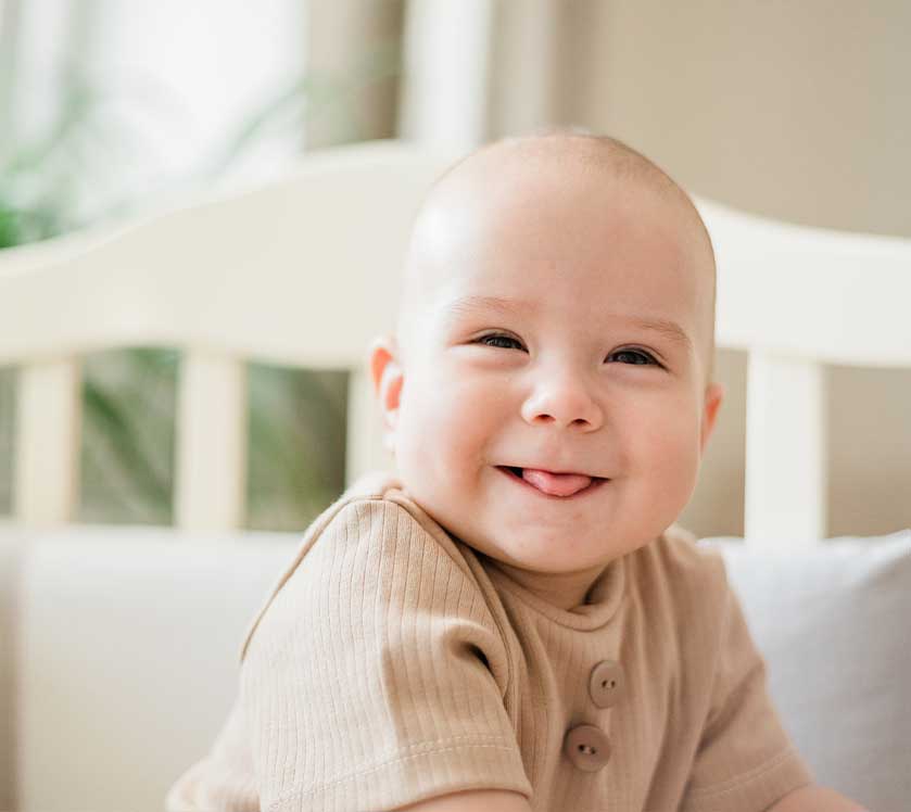 Baby smiling in a crib with a neutral background
