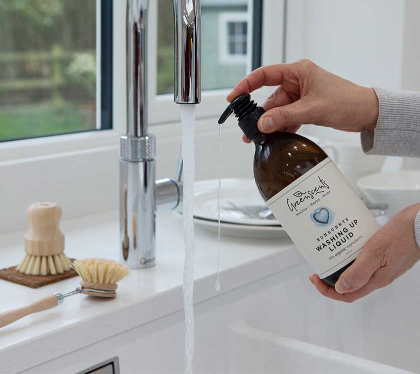 Person holding a bottle of greenscents washing-up liquid over a sink.