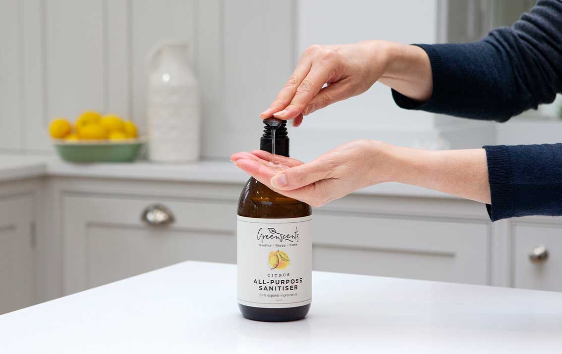 Person using a bottle of greenscents All Purpose Sanitiser on a kitchen counter.