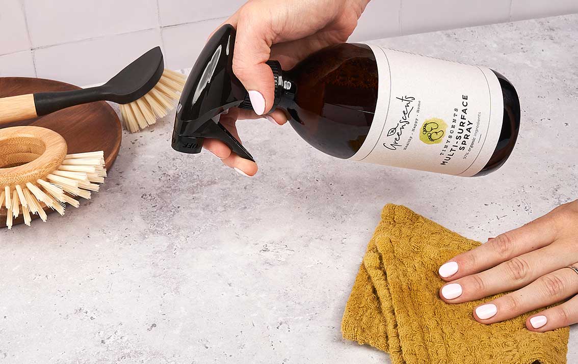 Person cleaning a greenscents  bottle with a brush and cloth on a kitchen counter.