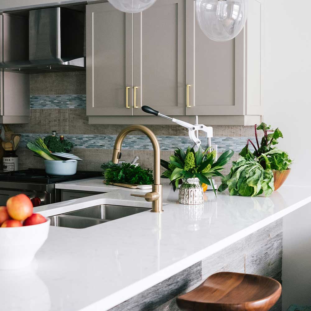 Modern kitchen with white countertops, stainless steel sink, and various kitchen items.