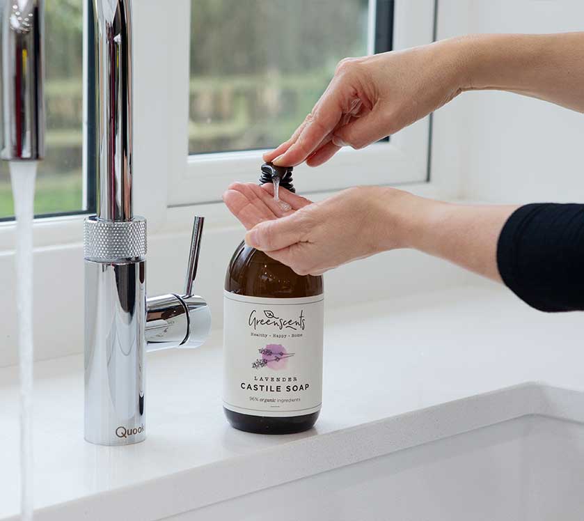 Person using a bottle of Greenscents Castile Soap in a kitchen setting.