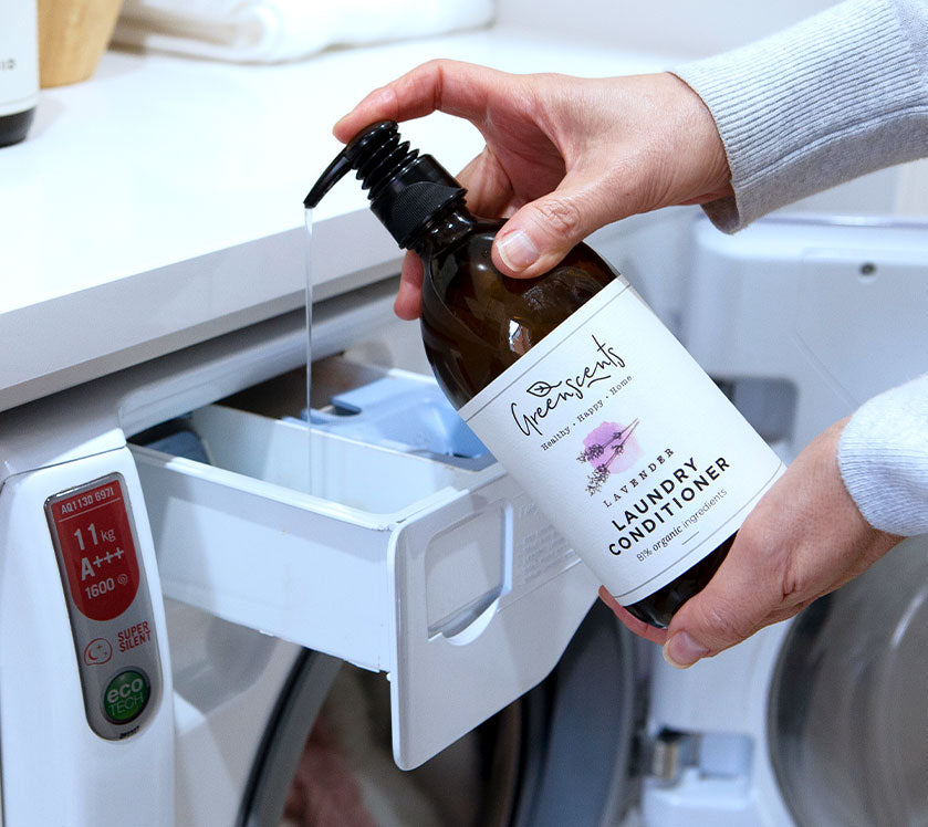 Person pouring greenscents  laundry conditioner into a washing machine