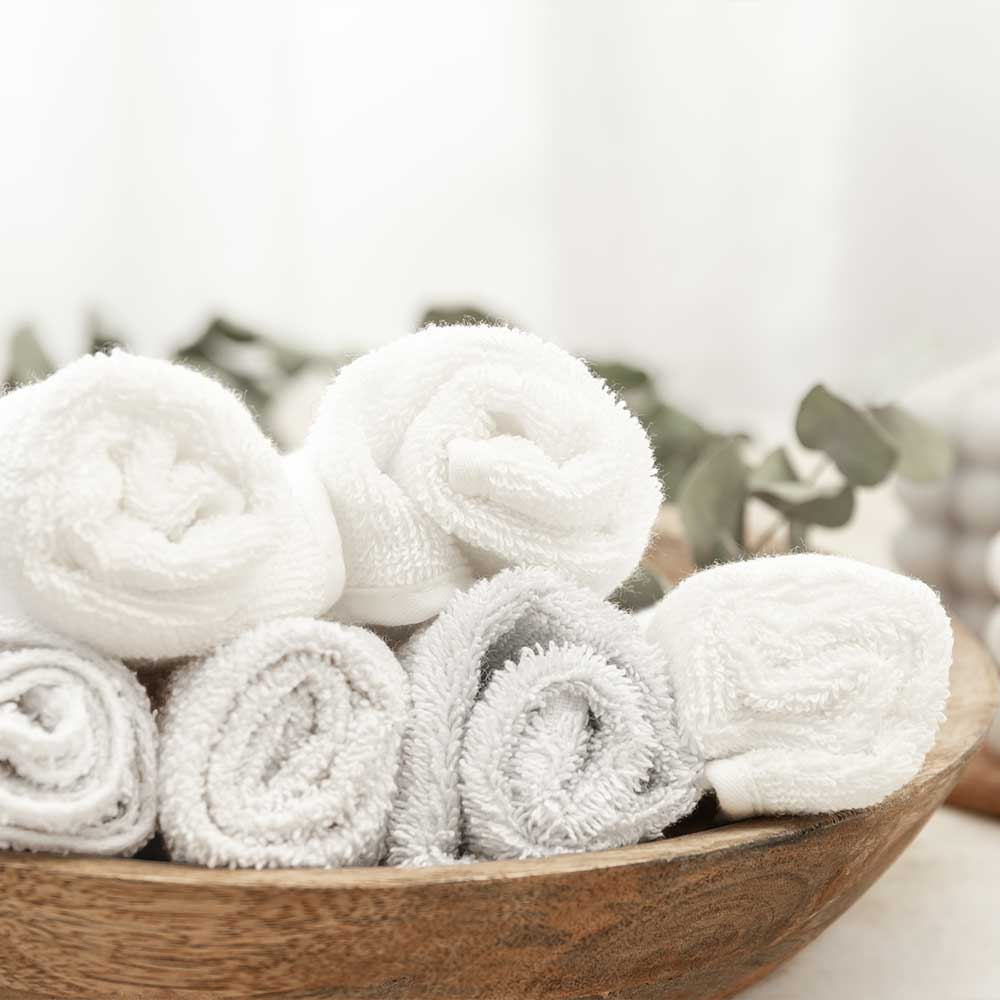 Wooden bowl filled with rolled-up white towels on a light background
