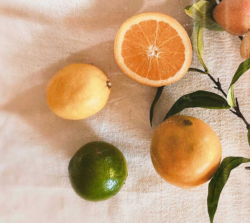 Citrus fruits including oranges, a lime, and a lemon on a textured surface.