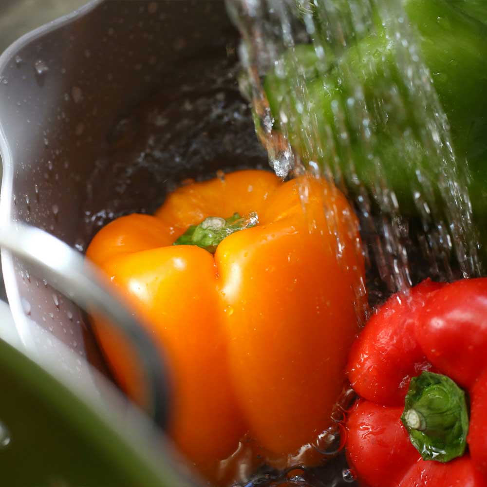 Peppers being washed under running water in a sink.
