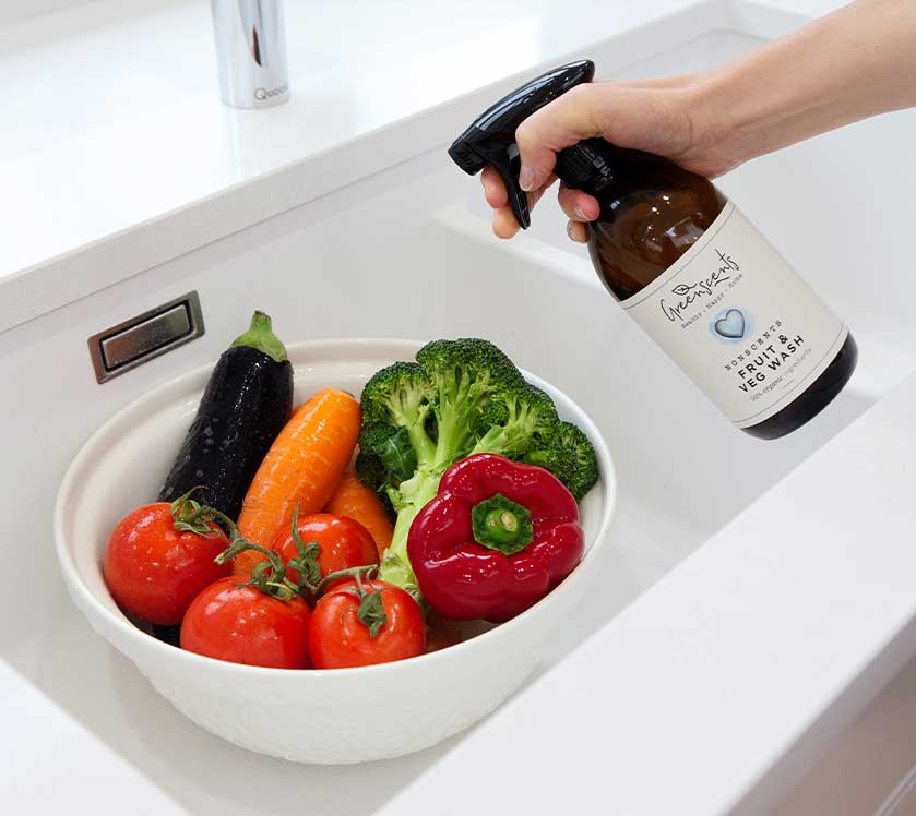 Person using a greenscents bottle of natural produce wash on vegetables in a sink.