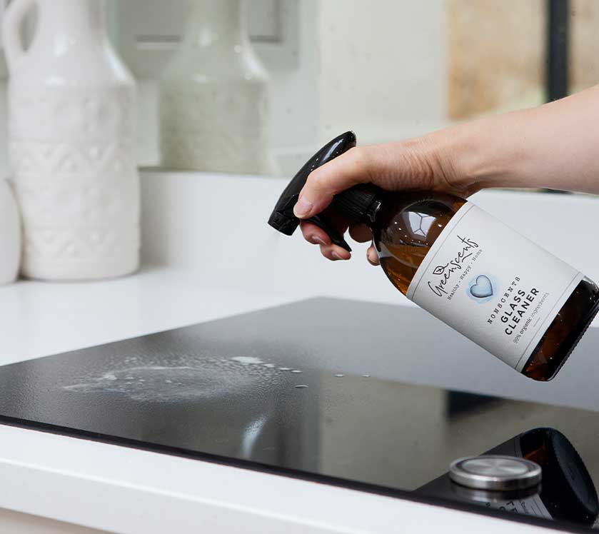 Person using a greenscents glass cleaner bottle on a stovetop