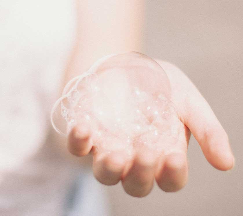 Close-up of a child's hand with greenscents soap bubbles on a neutral background