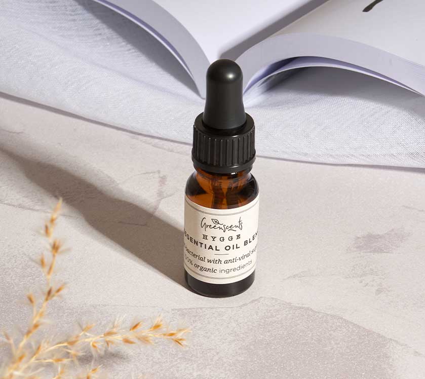greenscents Essential oil dropper bottle on a light surface with an open book in the background