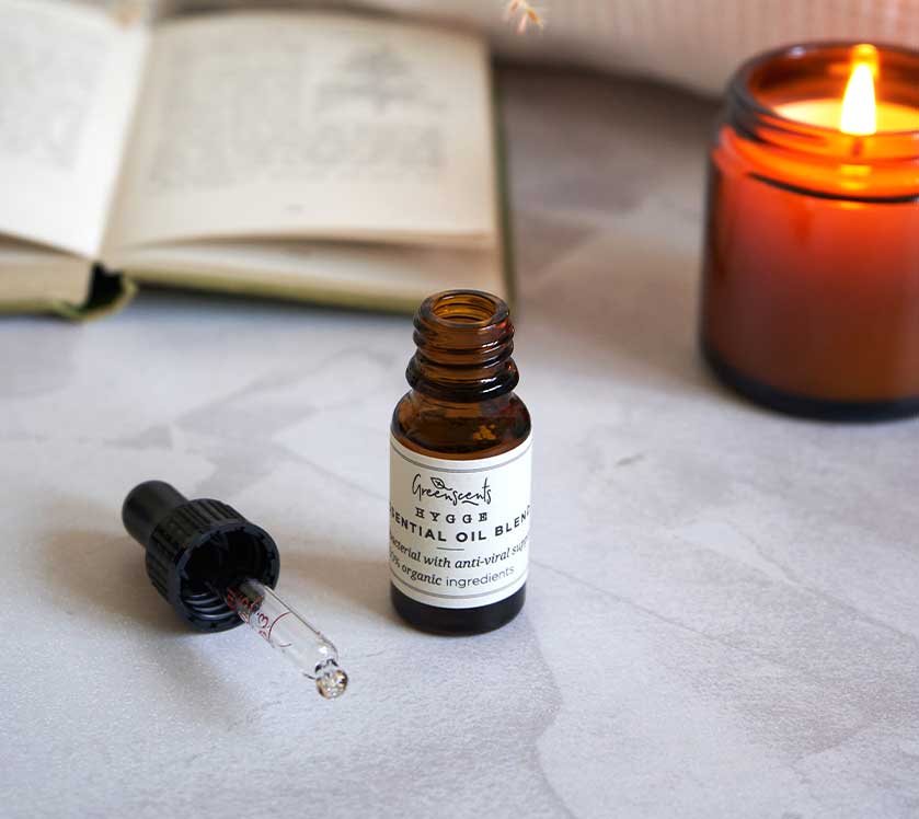 Bottle of greenscents essential oil blend with dropper on a textured surface next to a lit candle and open book.