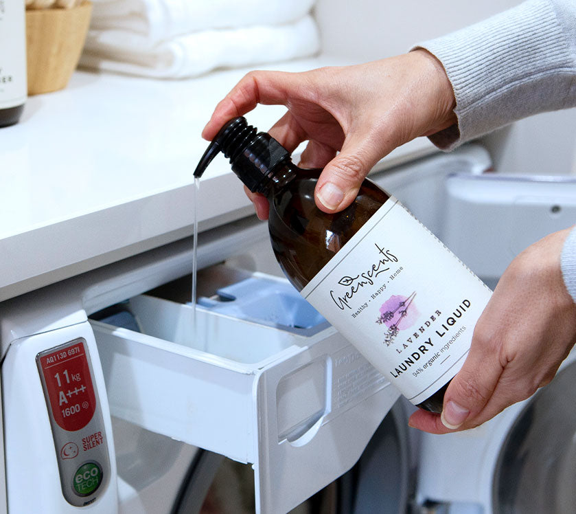Person pouring greenscents  laundry liquid from a bottle into a washing machine.