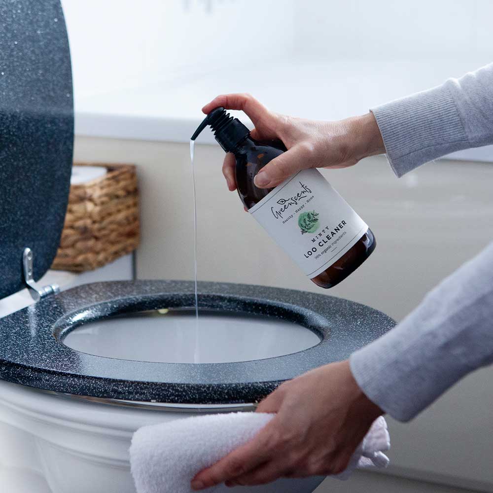 Person cleaning a toilet with a bottle of eco-friendly toilet cleaner.