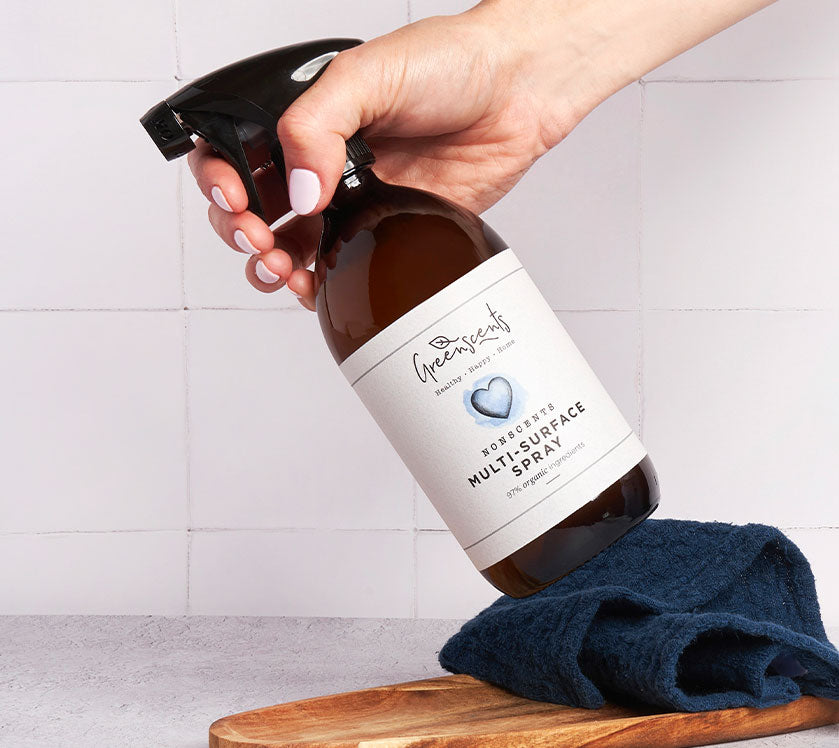 Hand holding a bottle of greenscents  multi-surface spray with a white tiled wall background