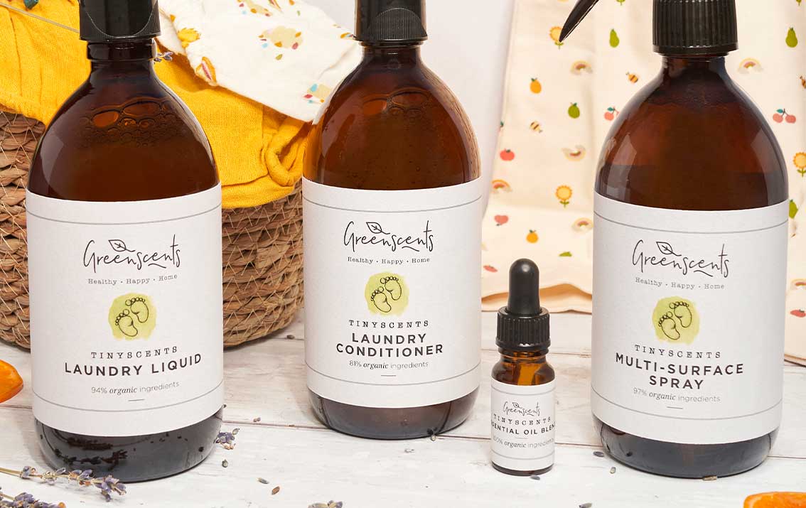 Set of GreenScents cleaning products including laundry liquid, conditioner, and spray on a wooden surface.