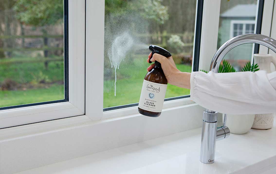 Person cleaning a window with a greenscents spray bottle in a bathroom setting