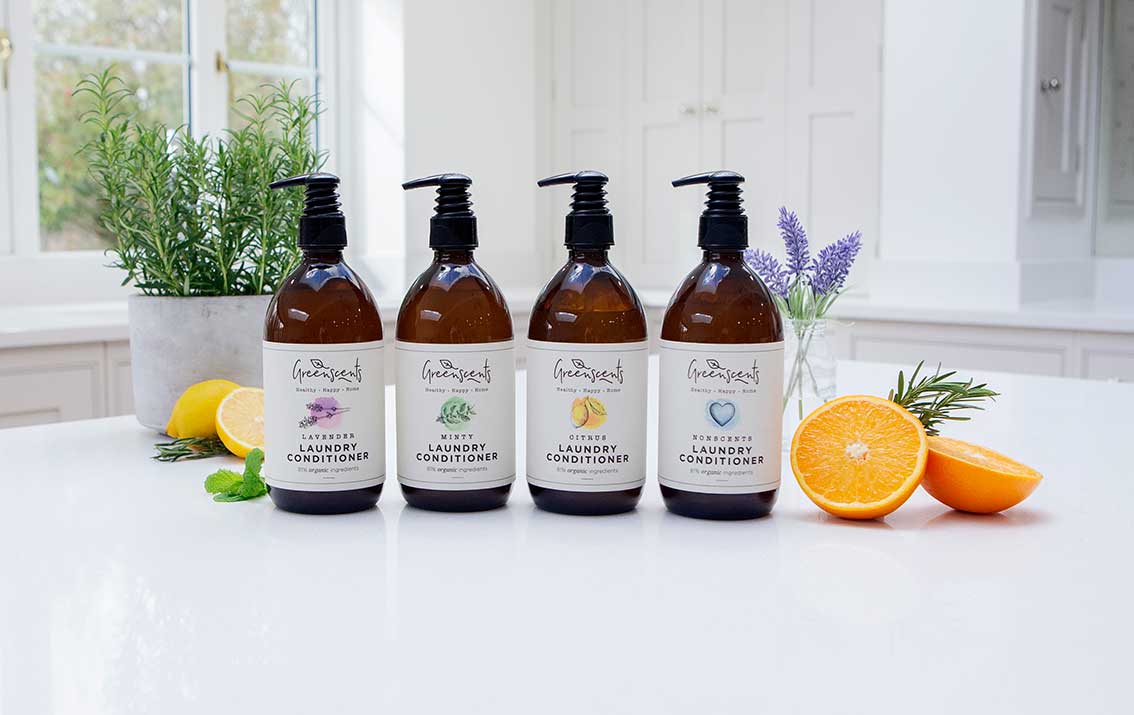Set of four bottles of 'greenscents ' conditioner on a white surface with fruits and plants.