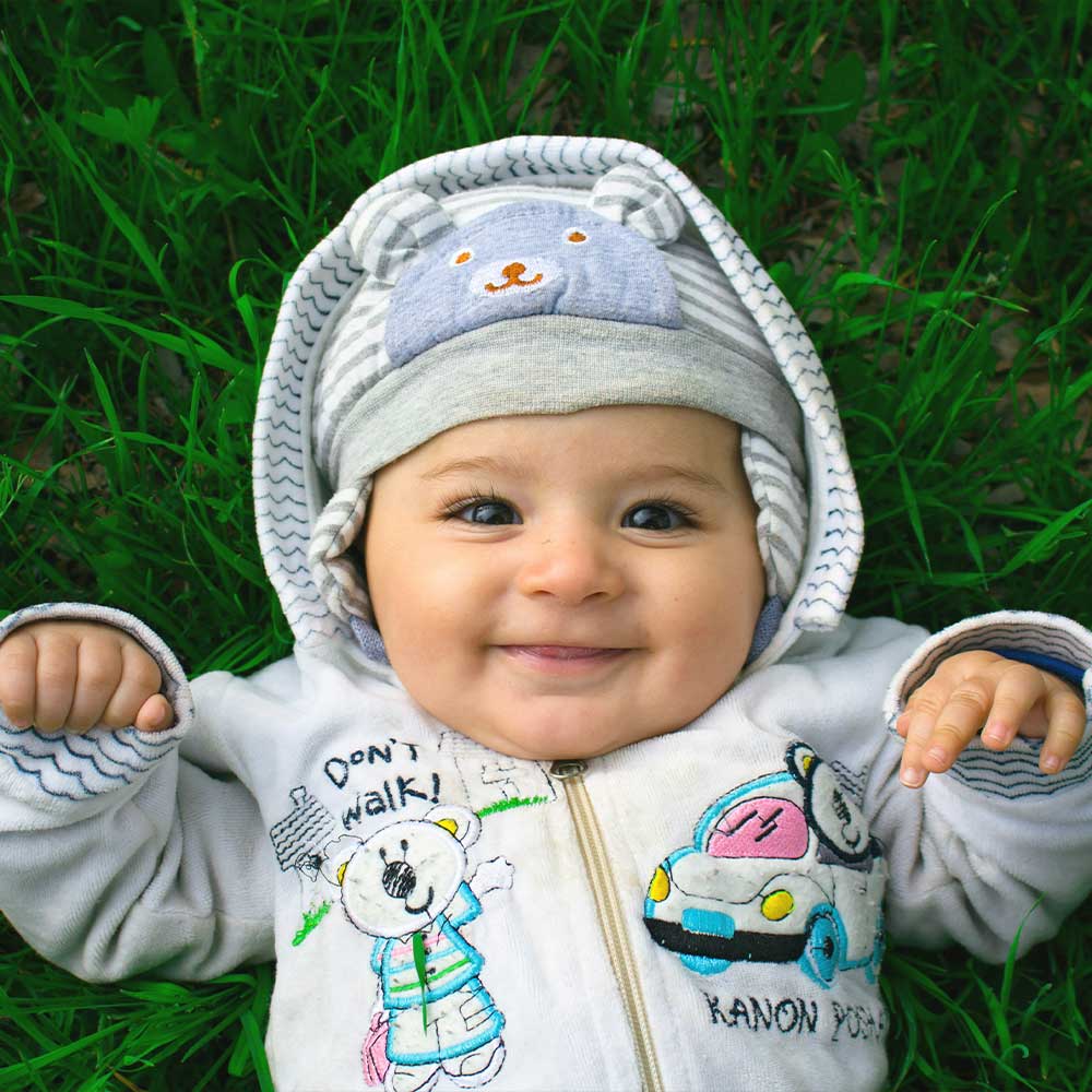Baby wearing a colorful jacket with cartoon designs, lying on grass